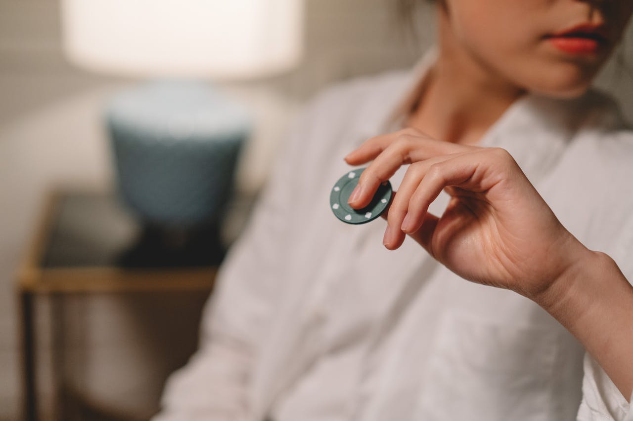 Close-up of a woman in a white blouse holding a poker chip with a blurred background, indoors.
