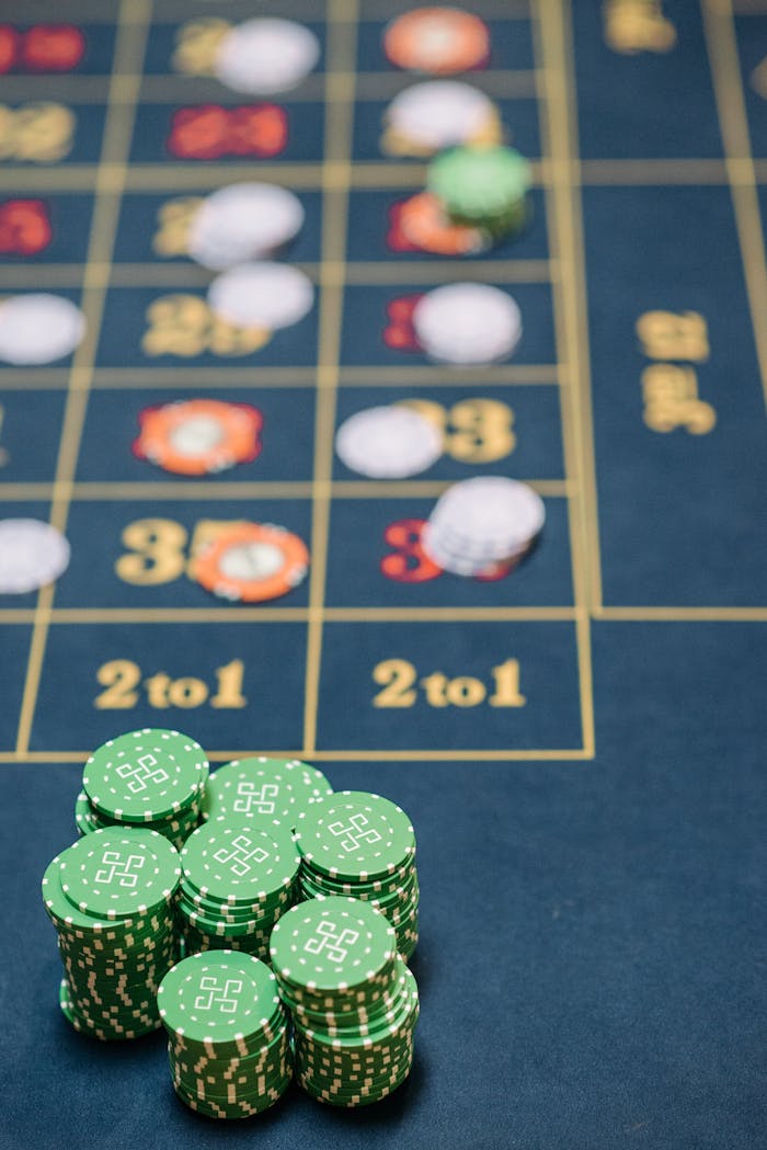 Green casino chips stacked on a roulette table with number layout and betting areas visible.