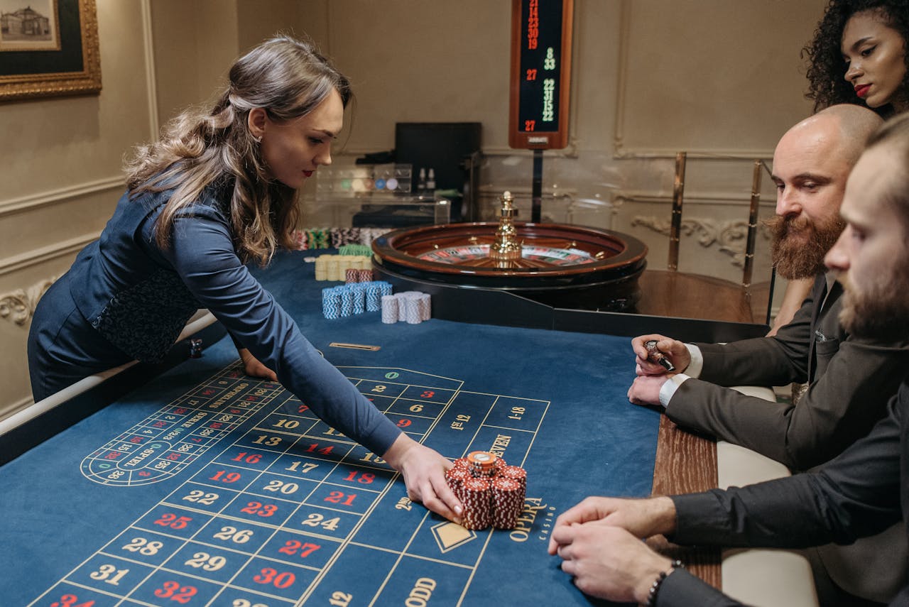 A group of people playing roulette at a casino with a female dealer organizing chips on the table.